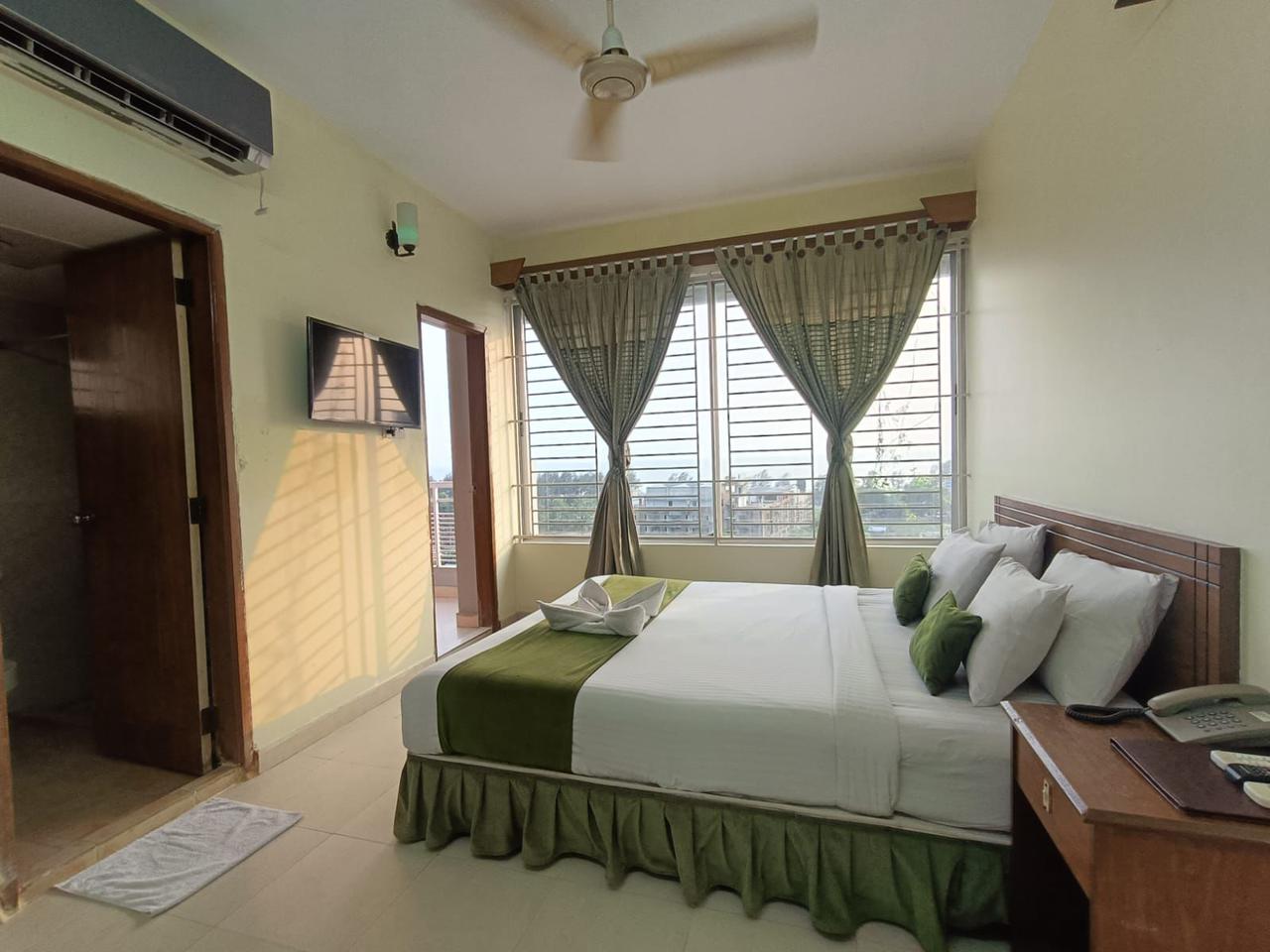 Hotel Room with Balcony Access and Natural Light Bright hotel room with a double bed, green curtains, and a large window offering a balcony view.