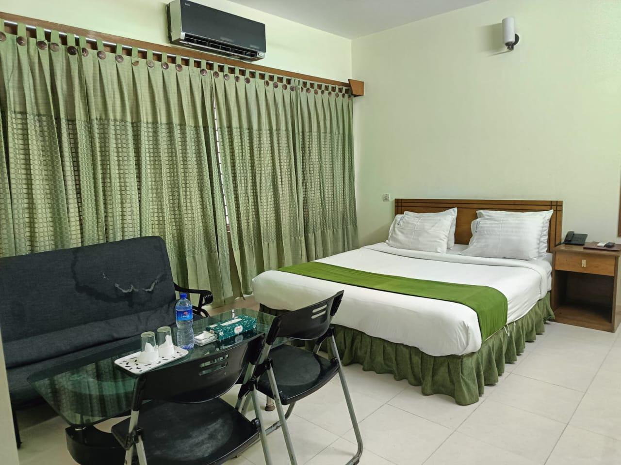 Comfortable Hotel Room with Seating Area Hotel room with a bed, green curtains, a black sofa, and a glass coffee table with chairs.