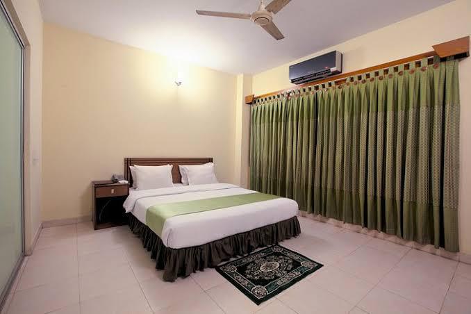 Modern Hotel Room with Glass Partition Spacious hotel room with a double bed, green accents, and a glass partition separating a sitting area.