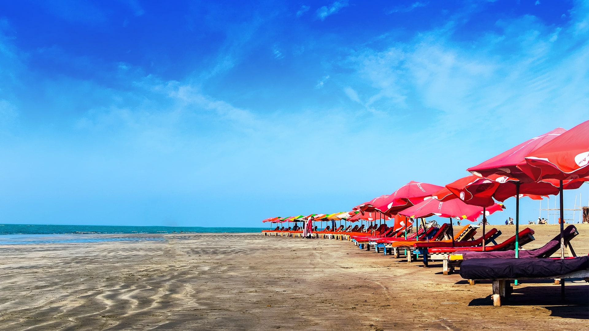 Colorful beach umbrellas and loungers on Cox’s Bazar sea beach under a clear blue sky.