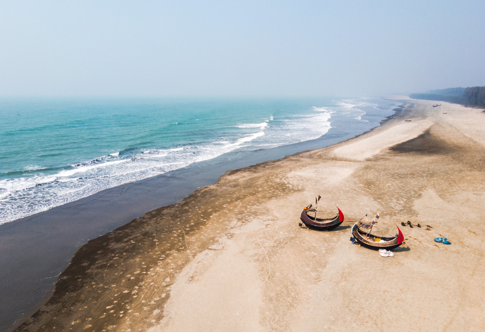 Scenic view of Cox's Bazar beach with fishing boats on the sandy shore and calm turquoise waters