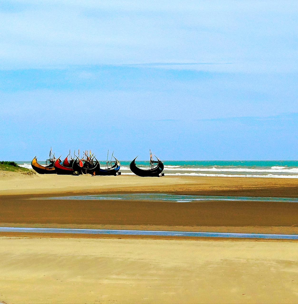 A serene beach with colorful traditional fishing boats lined up on the shore, with the turquoise ocean in the background.